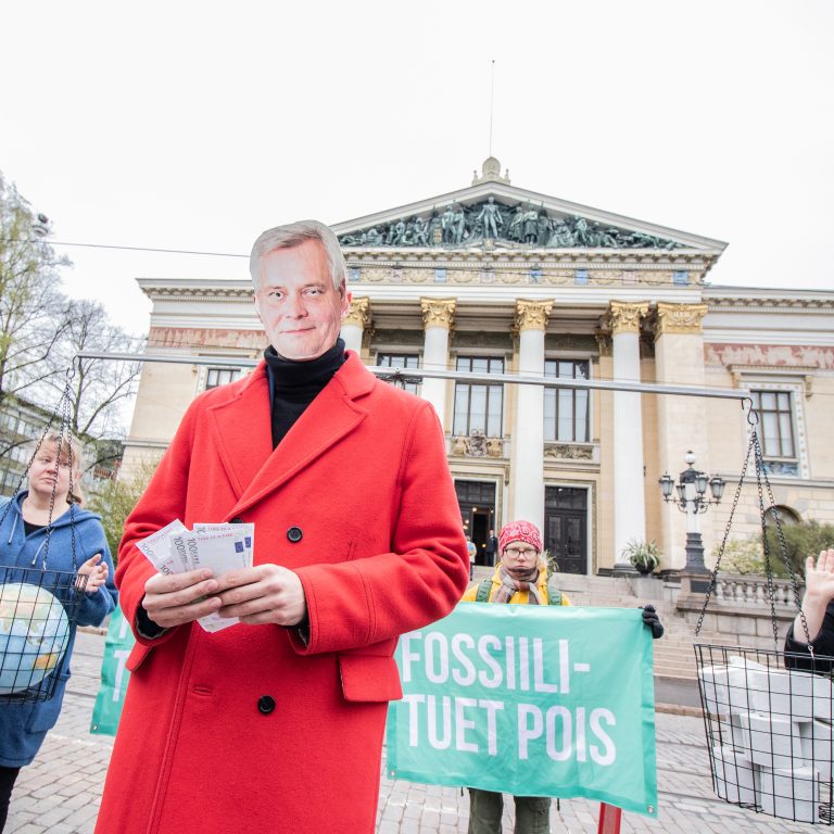 Antti Rinteeksi pukeutunut aktivisti pitelee seteleitä Säätytalon edellä järjestötempauksessa.