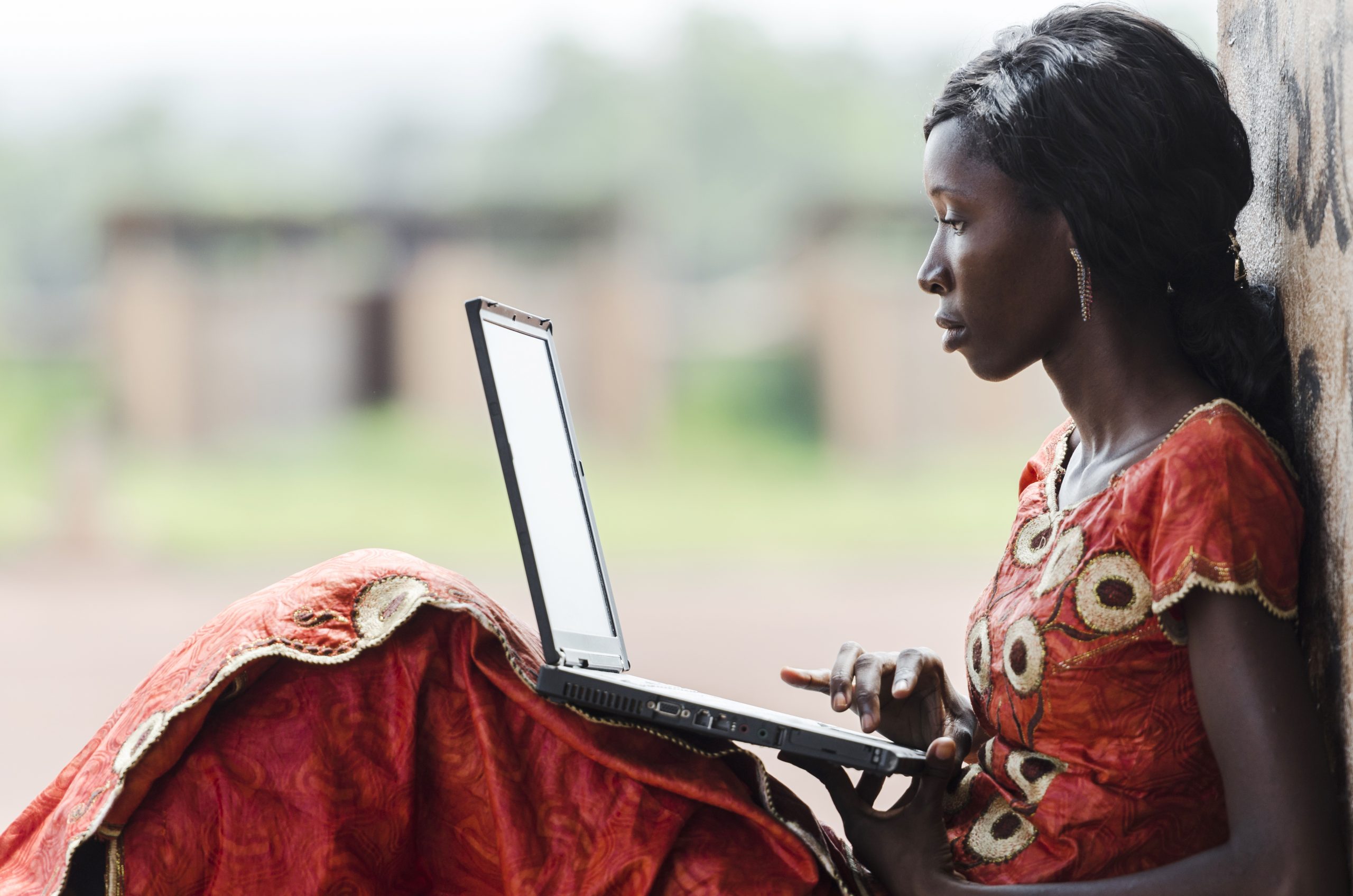 afrikkalaisnainen pitelee kannettavaa tietokonetta polvillaan