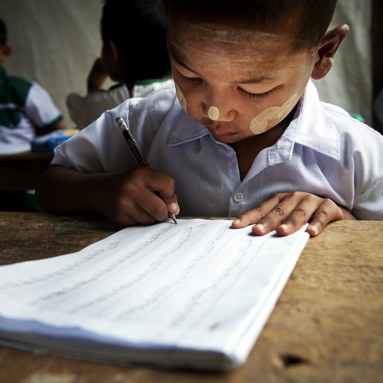 myanmarilaispoika kirjoittaa pulpetin äärellä paperille