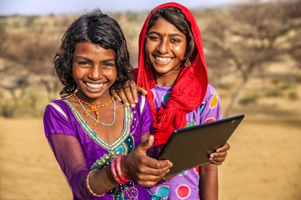Young girls sitting on a sand dune and using digital tablet in desert village, Thar Desert, Rajasthan, India.