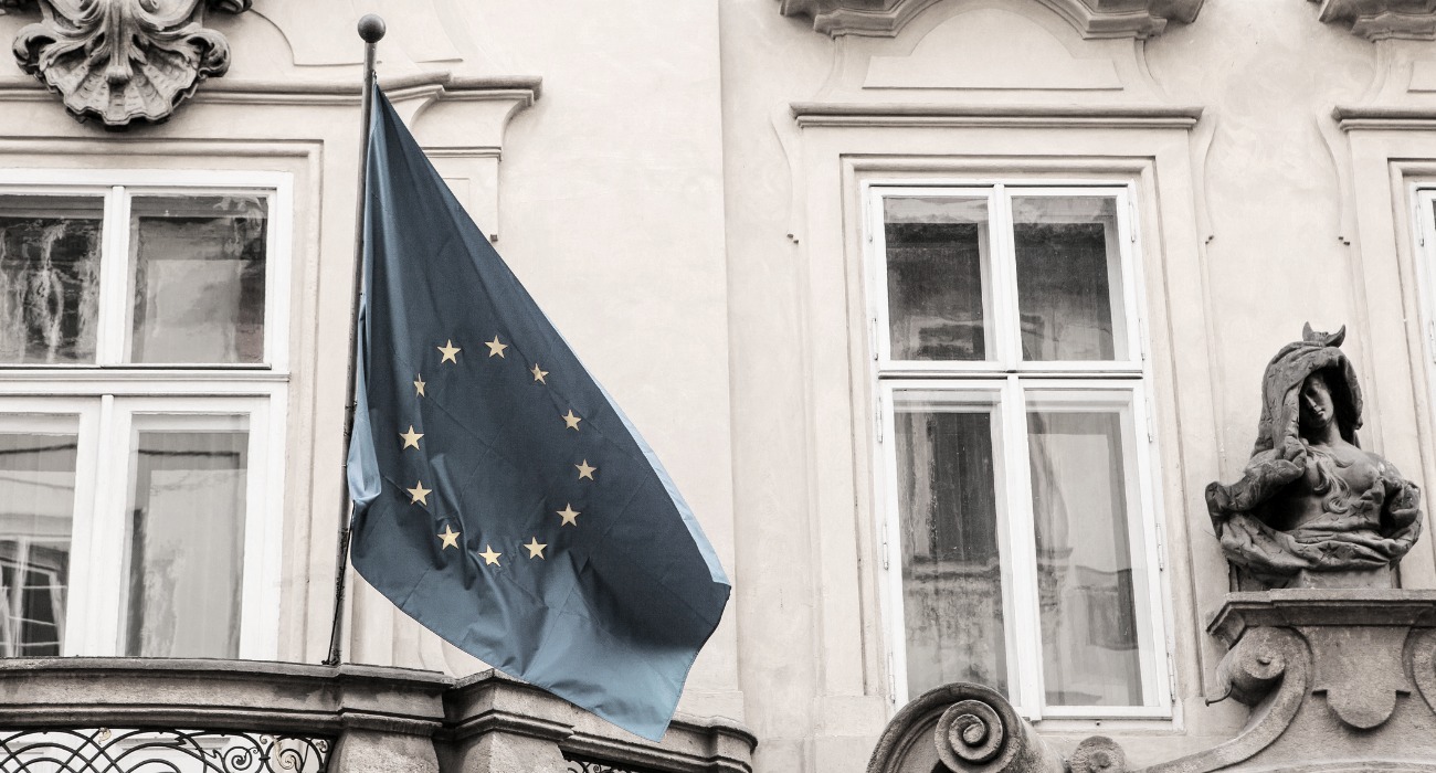 Mustavalkoinen kuva EU-lipustav roikkumassa lipputangossa rakennuksen seinällä.