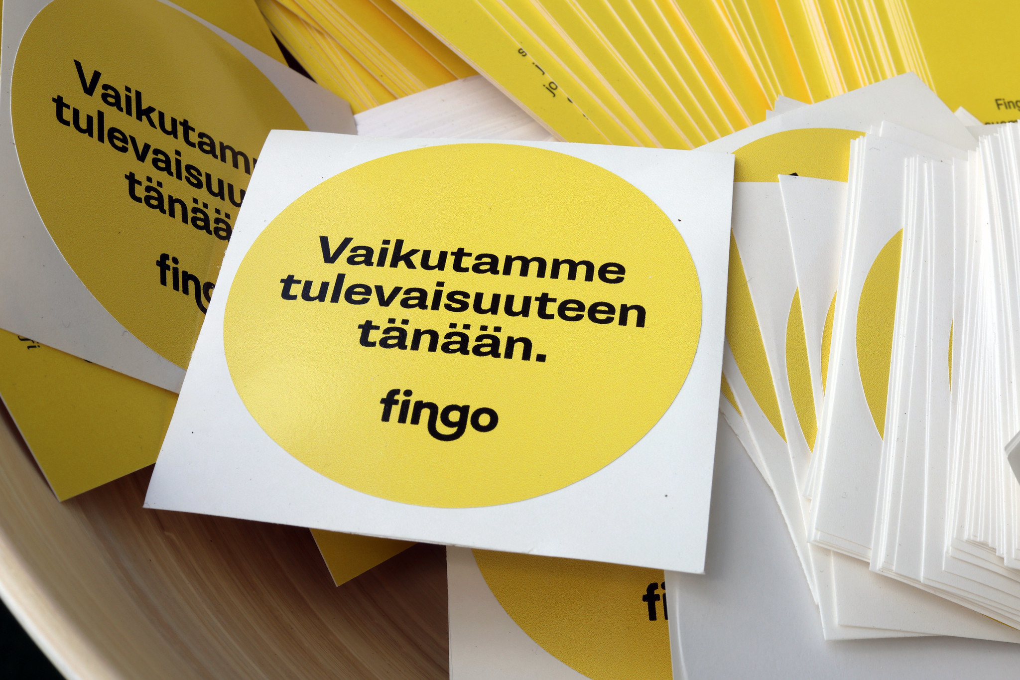 Fingon keltaisia tarroja, joissa Fingon musta logo ja teksti Vaikutamme tulevaisuuteen tänään.