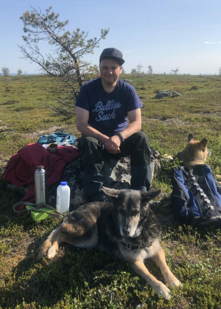 Sami Säynevirta istuu kivellä Tsarmitunturin erämää-alueella kahden koiran ympäröimänä.