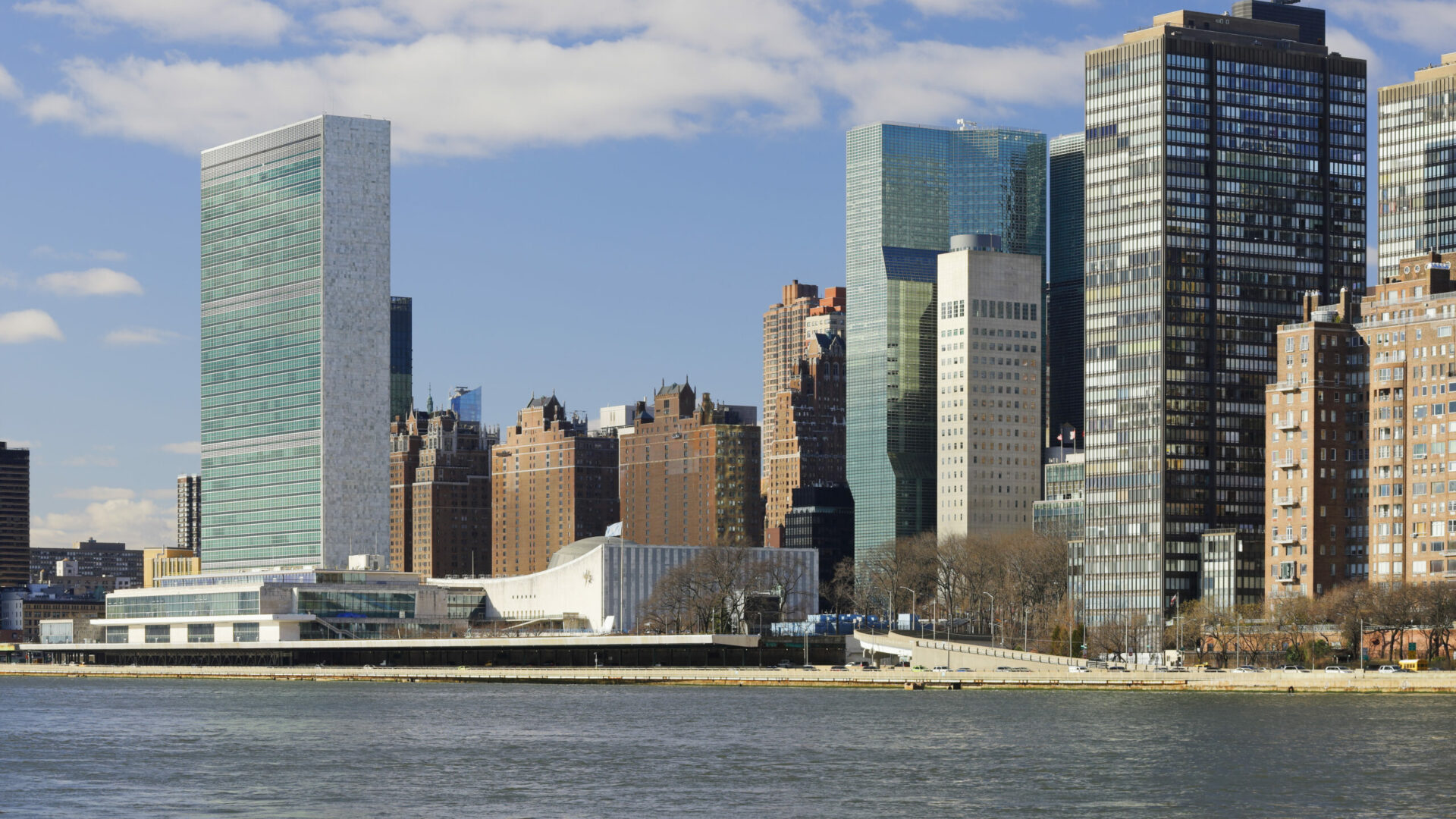 Kuvassa laajakuva, jossa näkyy YK:n päämaja ja New Yorkin pilvenpiirtäjiä.