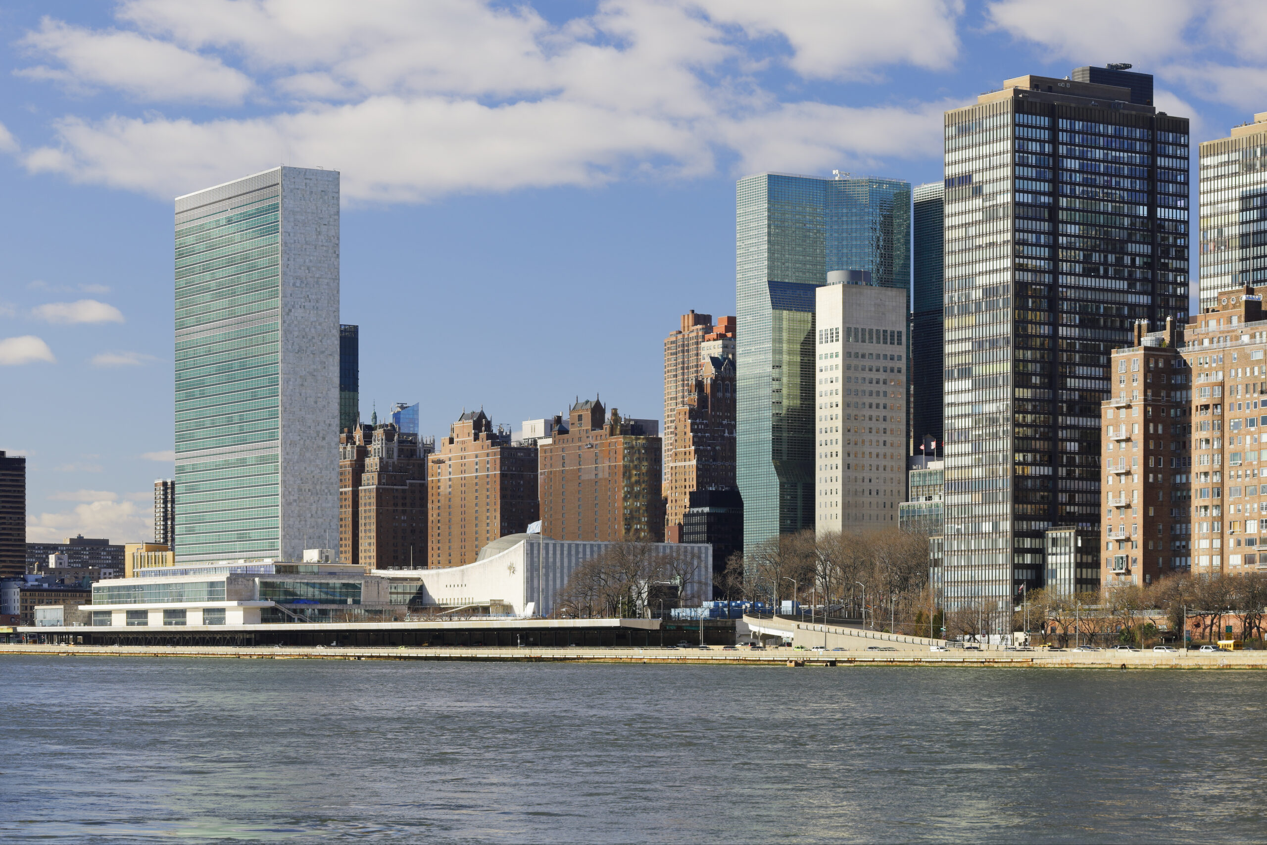 Kuvassa laajakuva, jossa näkyy YK:n päämaja ja New Yorkin pilvenpiirtäjiä.