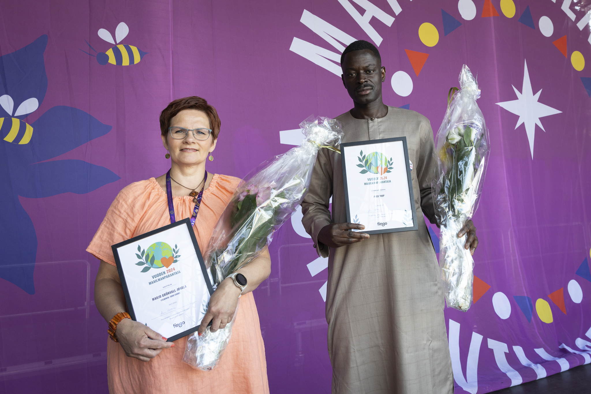 Marjo Grönvall-Jokela ja Paco Diop festivaalin musiikkilavalla kukat ja kunniakirjat käsissä.