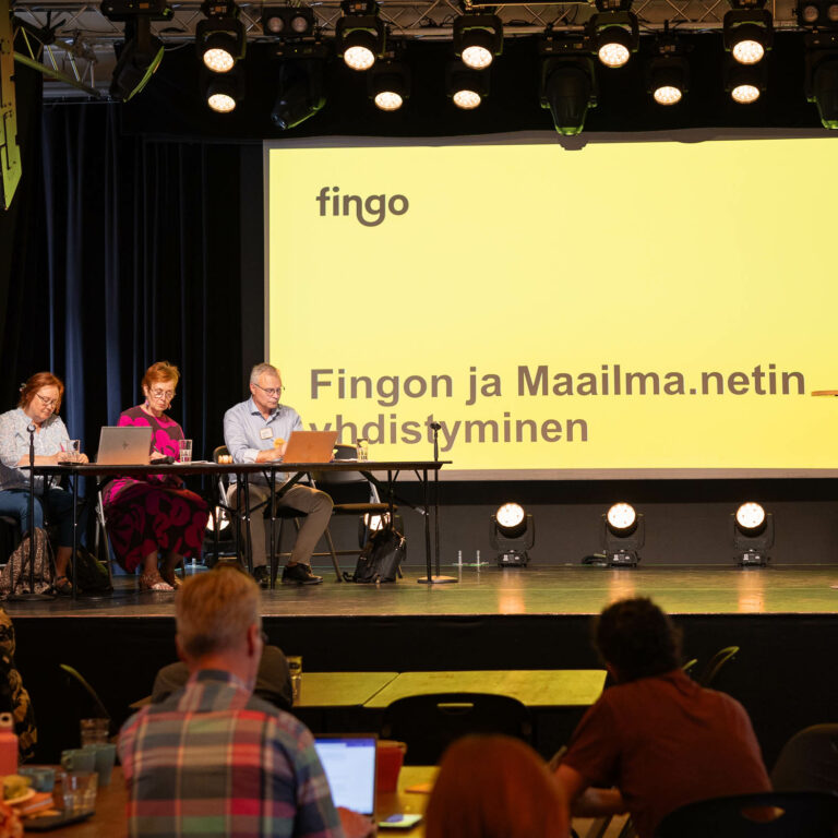 Kuvassa Fingon kevätkokouksessa käsitellään Fingon ja Maailma.netin yhdistymistä. Kuvassa kokouksen puheenjohtajistoa ja yleisöä.