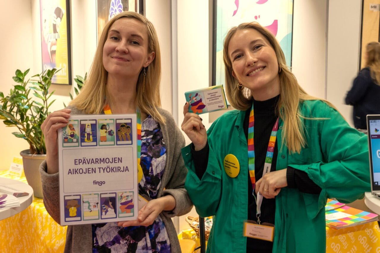 Fingon ständillä Educassa kaksi henkilöä esittelee ständin materiaaleja.