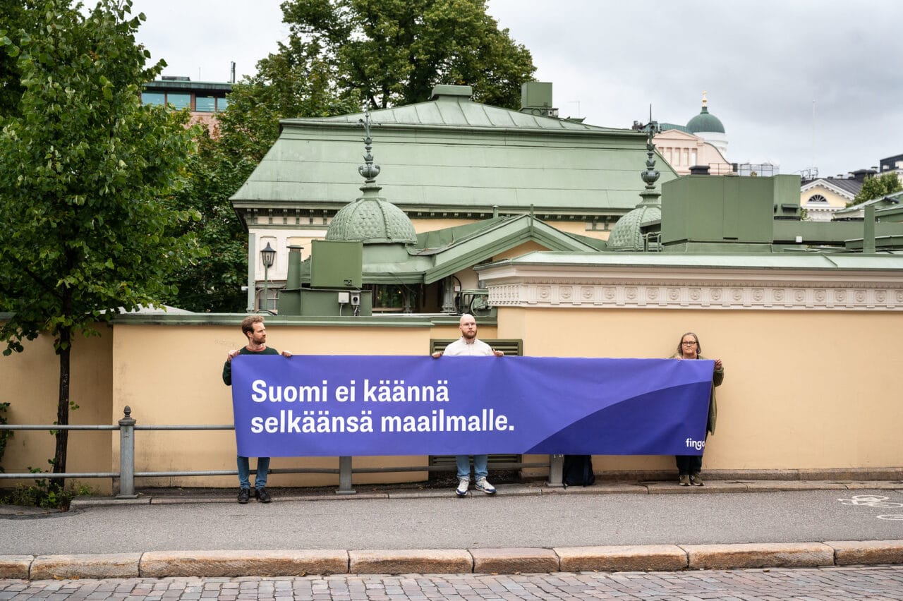 Kolme ihmistä pitelee banderollia