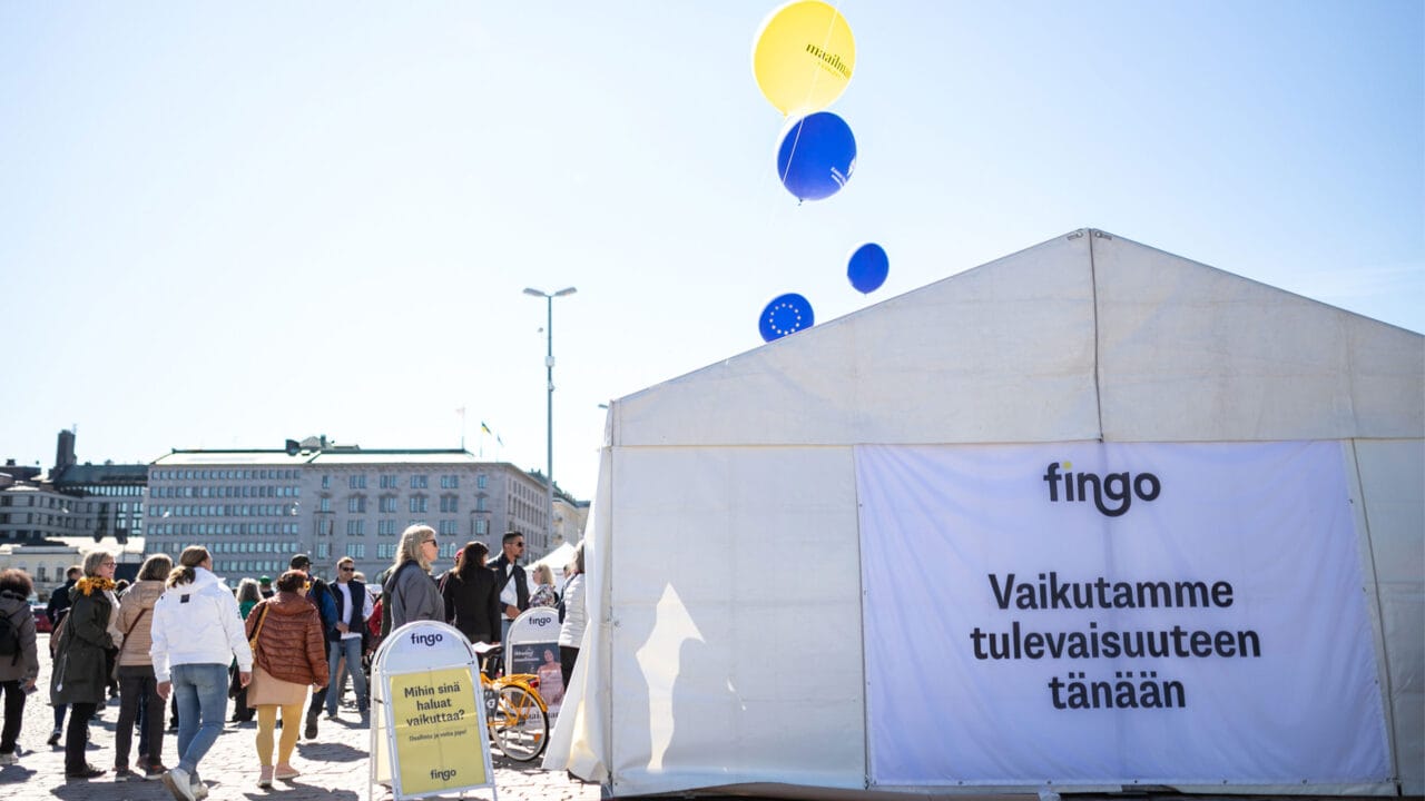 Fingon teltta Maailma kylässä -festivaaleilla vuonna 2022.|Fingon plakaatti Maailma kylässä -festivaaleilla. Plakaatissa lukee: Mihin sinä haluat vaikuttaa?