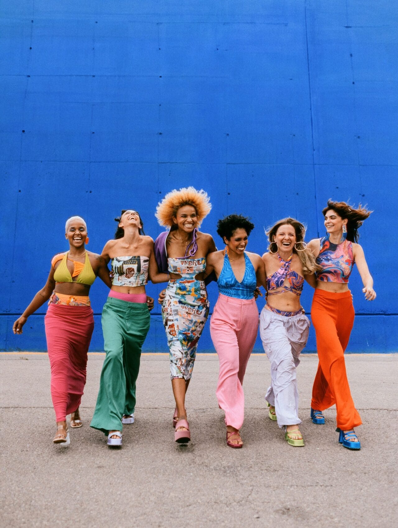 Six women in colorful clothes walk hand in hand