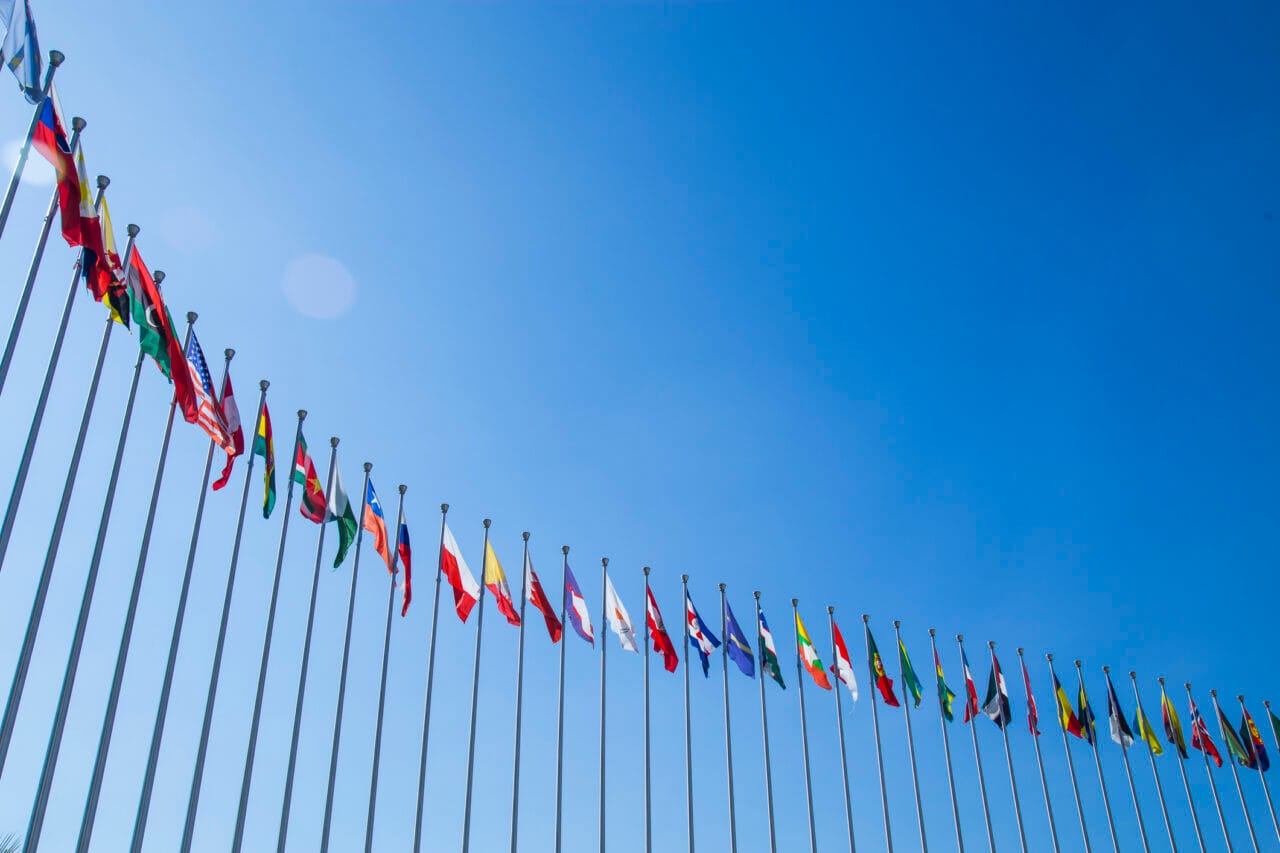 Maailman valtioiden lippuja liehuu tuulessa. Taustalla sininen taivas.