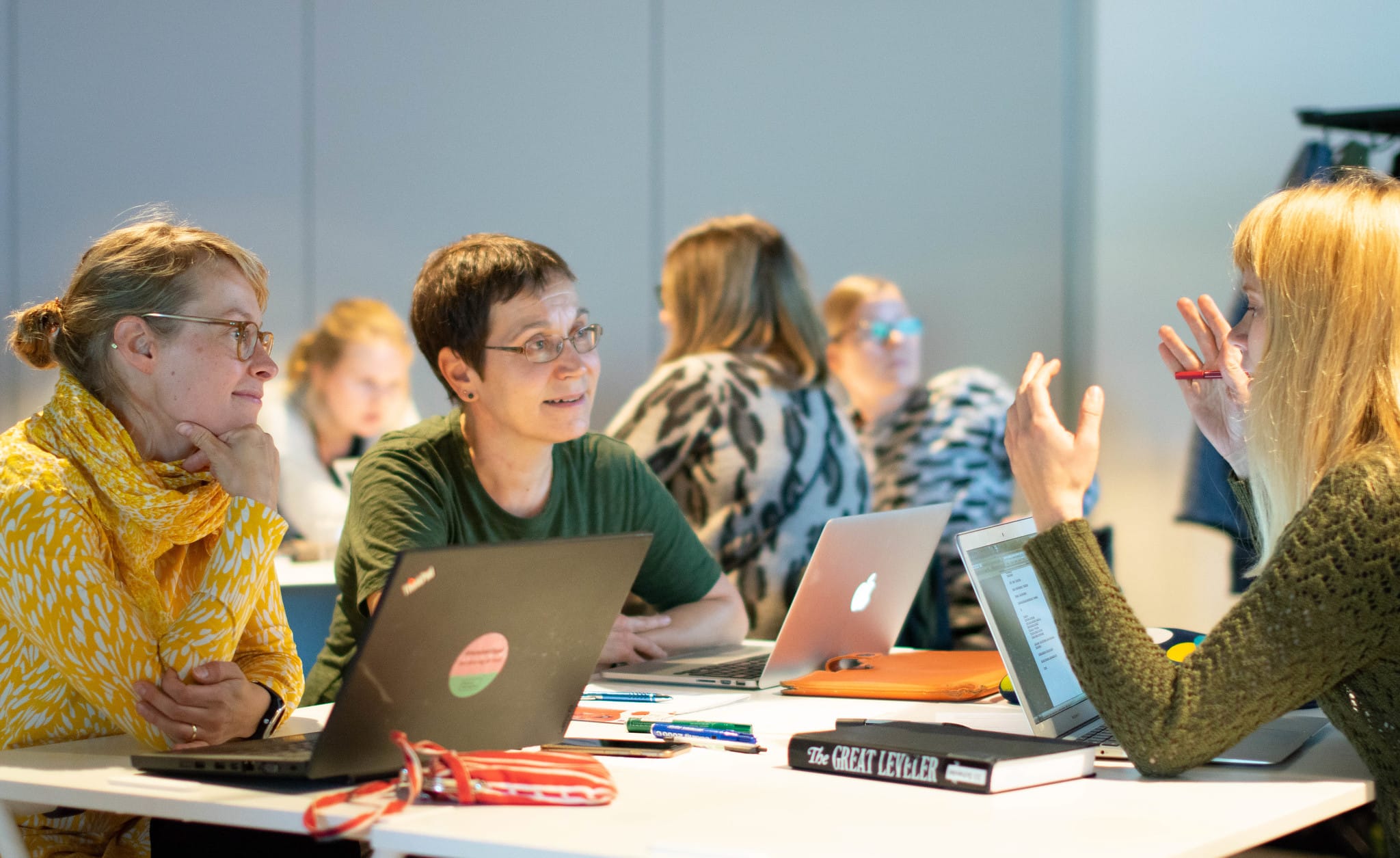 Henkilöt istuvat pöydän äärellä läppärit auki.