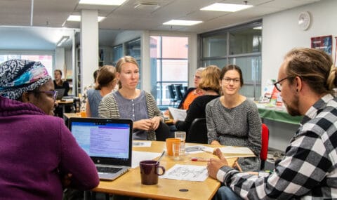 Henkilöt istuvat pöydän ääressä koulutuksessa.